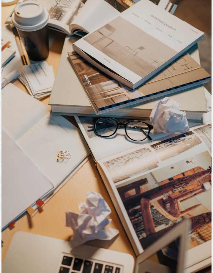 A laptop rests on a pile of magazines, open notes and reminders.